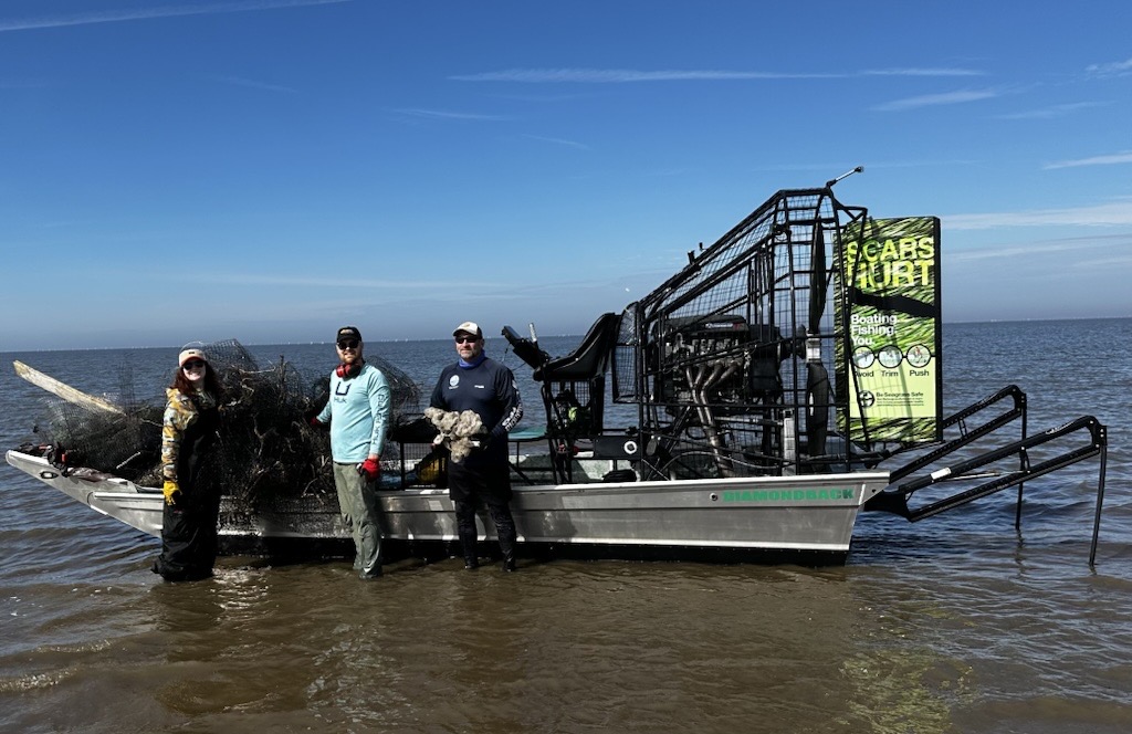 Cedar Key volunteer cleanup image of an airboat in water with people in front of collected marinedebris 