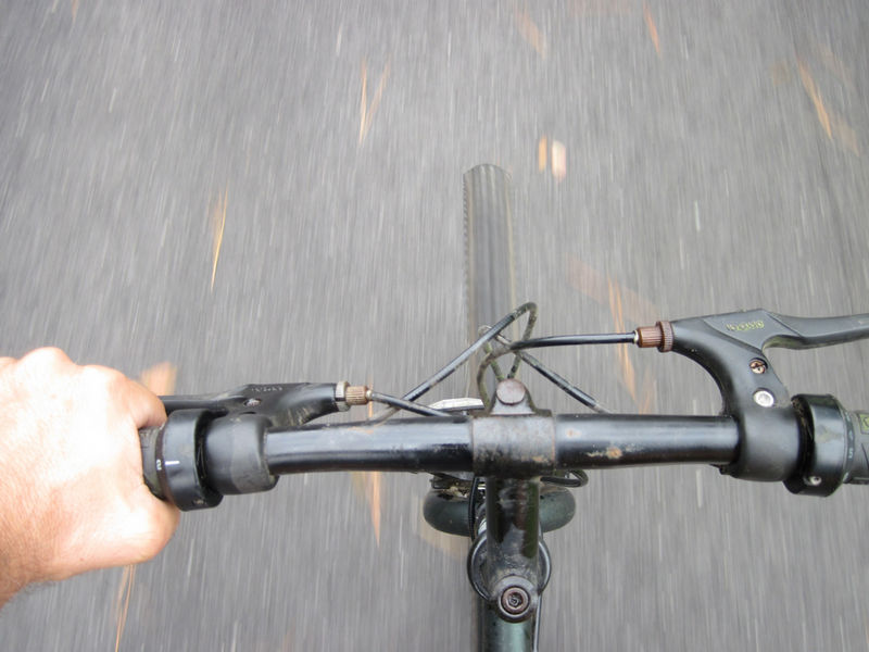 Perspective view of a biker looking down at their handlebars and the paved trail